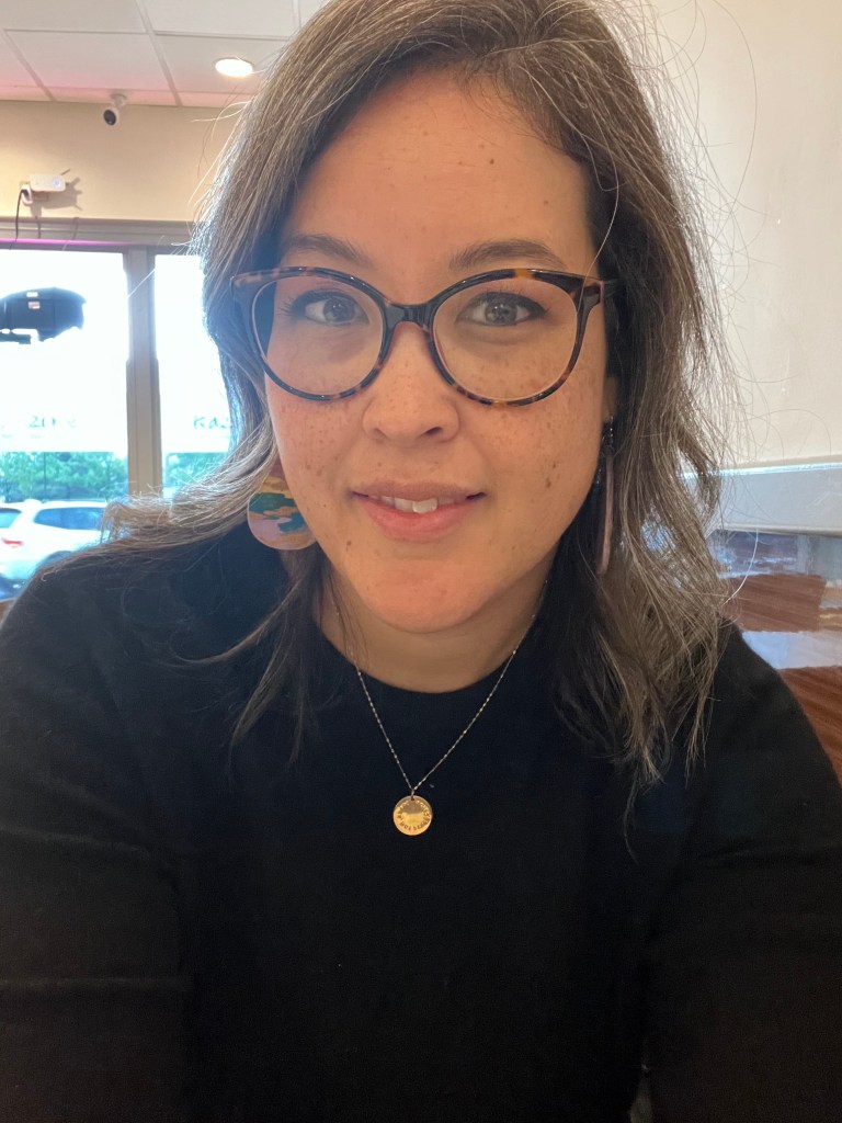 Image of Crystal Varner Parker wearing glasses, rainbow earrings, gold necklace, and black shirt